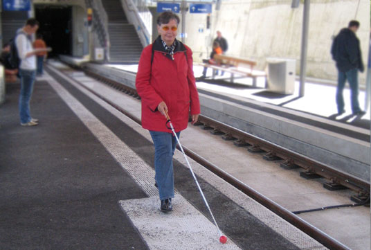 Nutzung von taktilen Leitstreifen zur Orientierung mit dem Langstock auf dem Bahnsteig.
