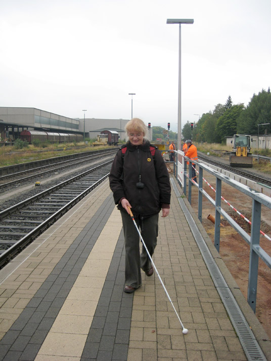 Nutzung von taktilen Leitstreifen zur Orientierung mit dem Langstock auf dem Bahnsteig.